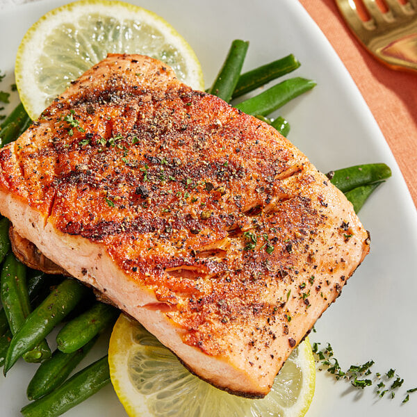 A plate of grilled salmon with lemon slices and green beans with a fork.