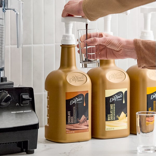 A large bottle of DaVinci Gourmet Chocolate Flavoring Sauce with a pump dispenser being used to pour sauce into a glass.