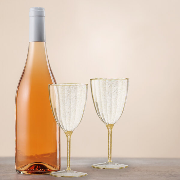 A bottle of wine and two Posh Setting gold glitter wine goblets on a table.