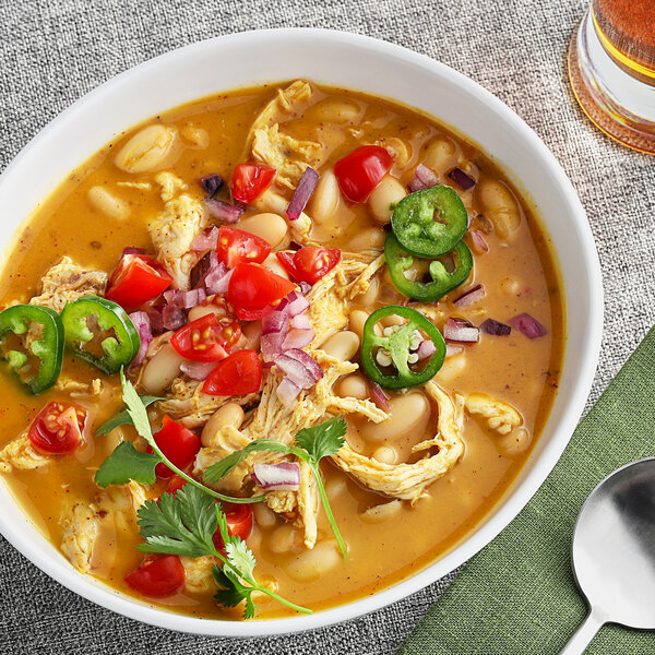 A bowl of soup with vegetables and meat next to a spoon.