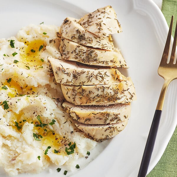 A plate of food with chicken, mashed potatoes, and thyme sprinkled on top with a fork and knife.