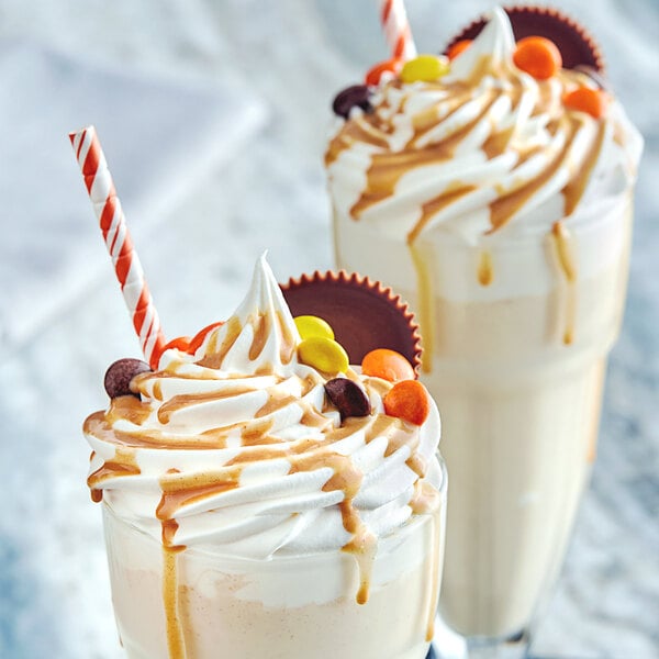 Two glasses of milkshakes with whipped cream and caramel toppings on a table in an ice cream shop.