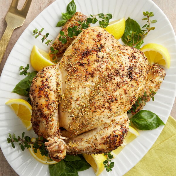 A whole chicken with Lawry's Lemon, Basil, and Thyme Key West-Style Seasoning, lemons, and herbs on a white plate.