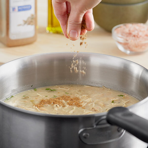 A person pouring McCormick Culinary Ground Cumin into a pot.