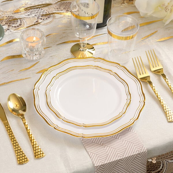 A table set with Posh Setting white plastic plates with gold bands and gold cutlery.