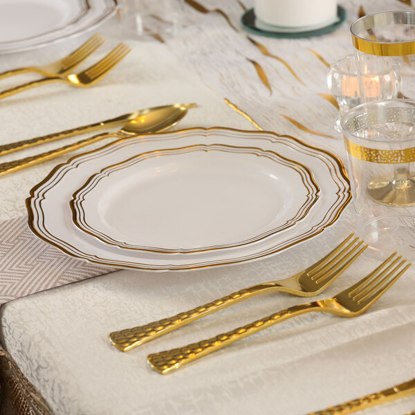 A table set with a Posh Setting white plastic plate with gold bands and gold forks.