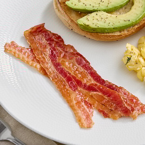 A plate with Daily's Applewood Smoked Bacon slices, avocado, and eggs on it.