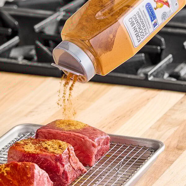 McCormick Culinary Korean BBQ Gochujang Style Seasoning being poured onto raw meat on a metal tray.