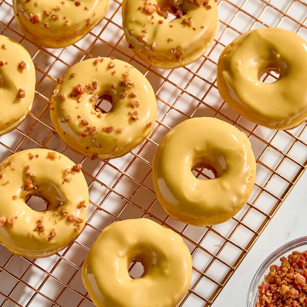 A batch of donuts with a glossy maple glaze, some topped with small crunchy bits, displayed on a cooling rack.