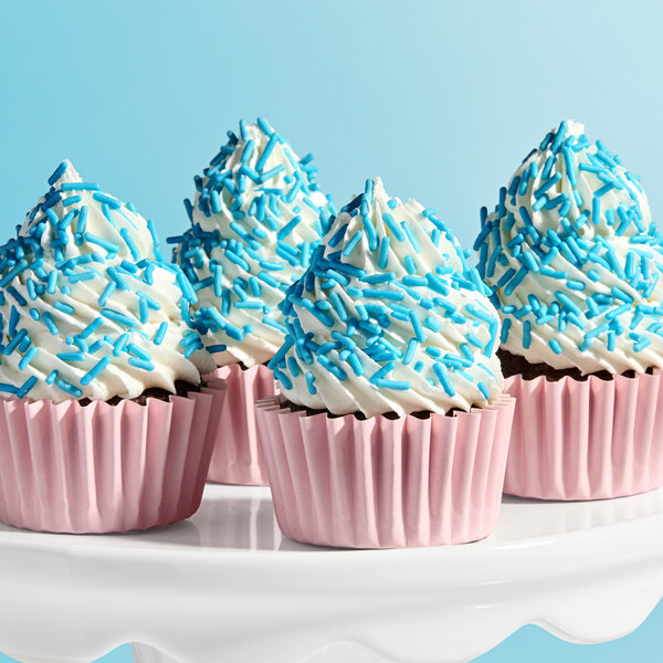 A group of chocolate cupcakes with white frosting and light blue sprinkles in pink paper liners.