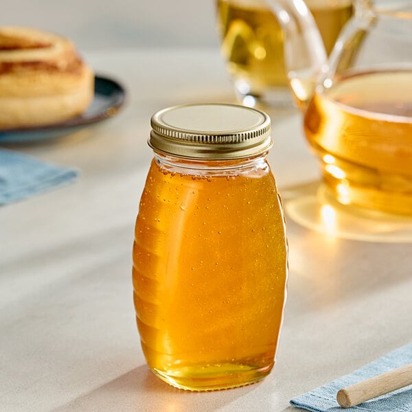 A Classic Queenline glass honey jar with a gold metal lid on a table.