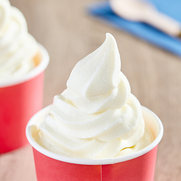 A close up of two red cups of Meadowvale vanilla soft serve ice cream with whipped cream on top.