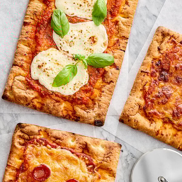 Three square pizzas topped with cheese, basil, and tomato sauce on a table.