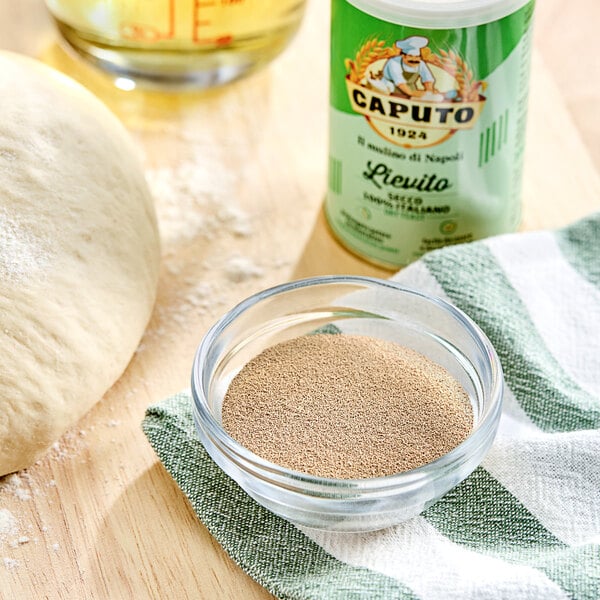 A bowl of dough next to a bowl of Caputo Lievito dry yeast and a bottle of olive oil.