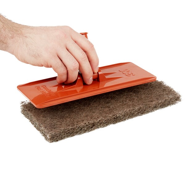 A hand using a red 3M Doodlebug scrub pad to clean a floor.