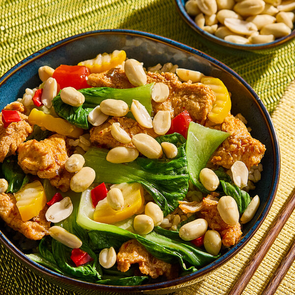 A bowl of stir-fried vegetables and protein garnished with blanched peanuts.