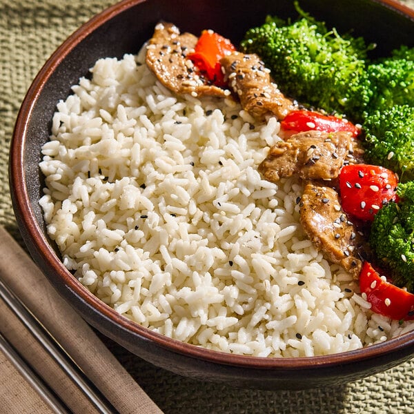 A bowl of cooked long grain white rice served with pieces of meat, broccoli, and red bell pepper.