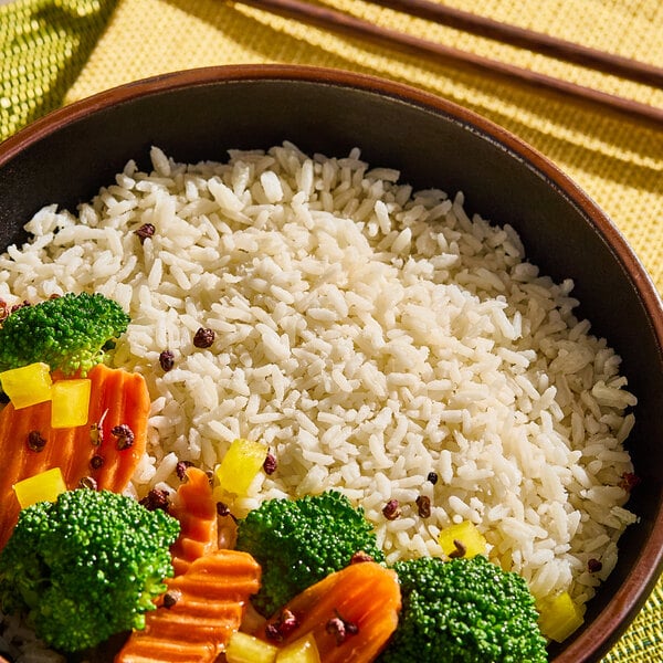 A bowl of cooked long grain white rice served with broccoli, carrots, and yellow bell peppers.