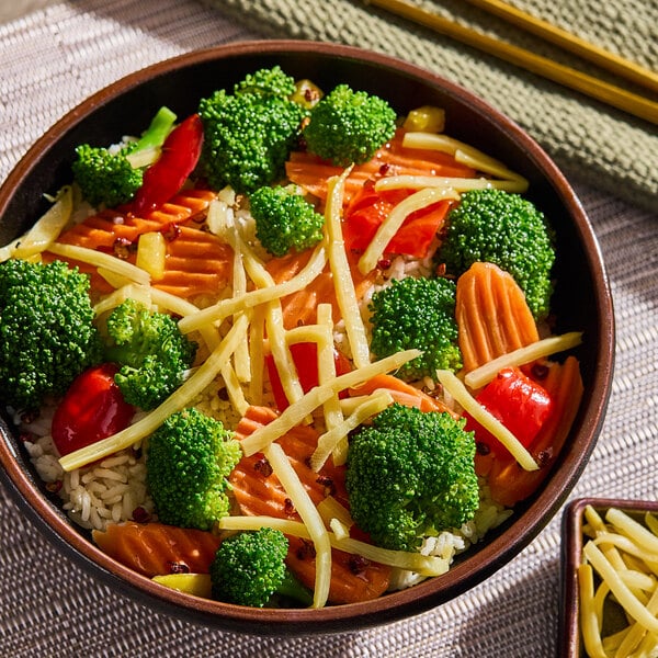 A bowl of rice topped with bamboo shoot strips, broccoli, carrots, and red bell peppers.