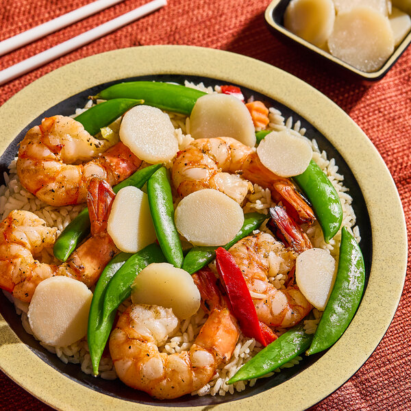 A plate of shrimp stir fry with sliced water chestnuts, snap peas, and rice.