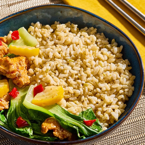 A bowl of cooked medium grain brown rice served with vegetables and pieces of tofu or chicken.