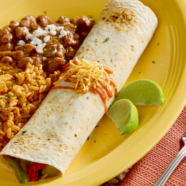 A large flour tortilla filled with ingredients, served with rice, beans, and lime wedges on a yellow plate.
