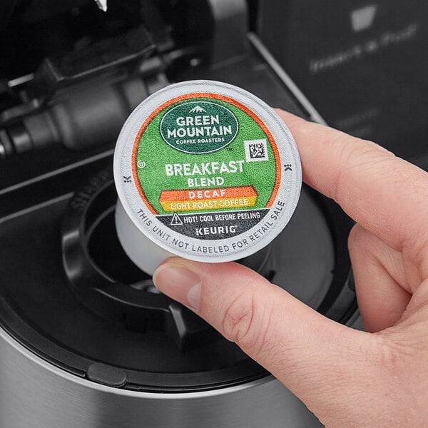 A hand holding a small round container of Green Mountain Coffee Roasters Decaf Breakfast Blend K-Cup Pods.