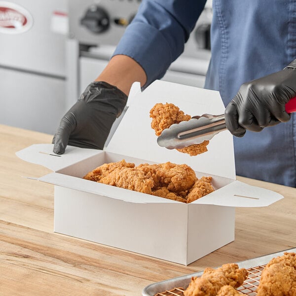 A white take-out lunch or chicken box with a handle being filled with fried chicken pieces.