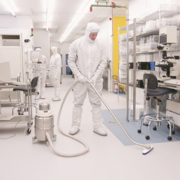 A man in white protective gear using a Nilfisk cleanroom vacuum to clean a room.