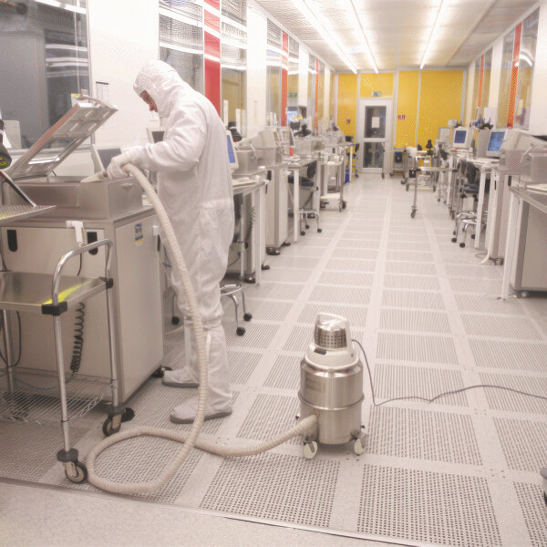 A man in a white suit using a Nilfisk stainless steel cleanroom canister vacuum.