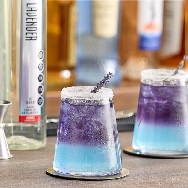 A glass of blue and purple liquid with lavender flowers on a table.