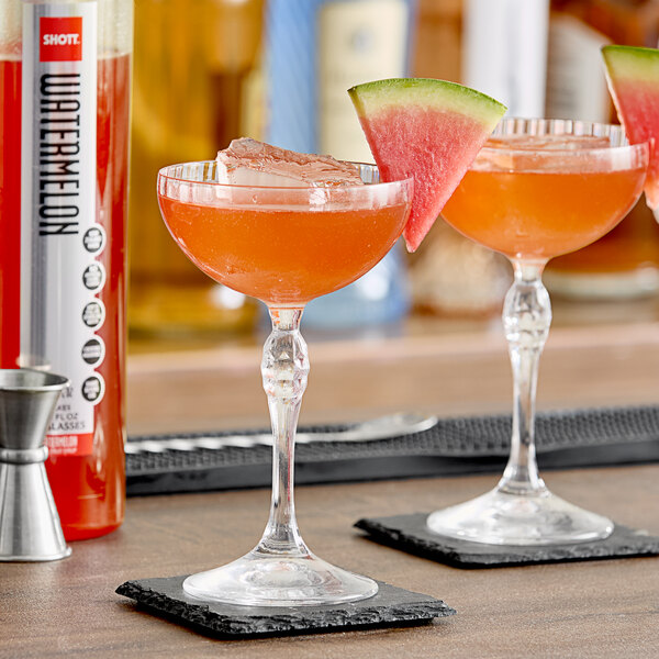A glass of watermelon and lime cocktail on a bar counter with a slice of watermelon next to it.