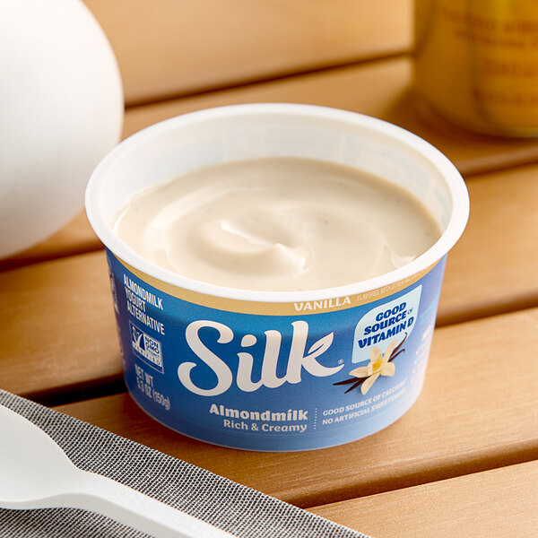 A container of Silk dairy-free vanilla almond milk yogurt alternative on a table.