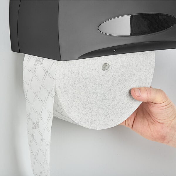 A hand holding a Scott Essential jumbo toilet paper roll.