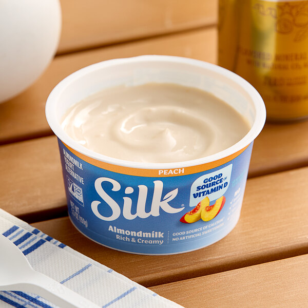 A container of Silk Dairy-Free Peach Almond Milk Yogurt Alternative on a table.