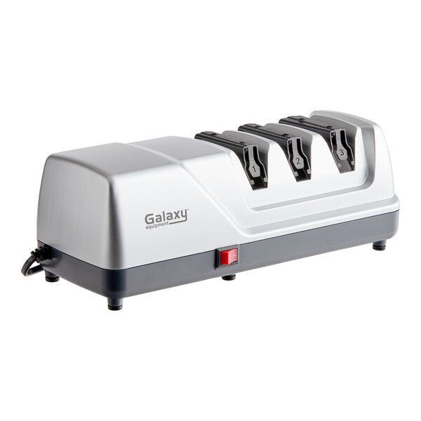 A silver and black electric knife sharpener with three sharpening slots and a red power switch.
