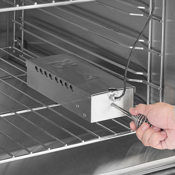 A stainless steel smoker box being placed inside a commercial cook and hold smoker oven.