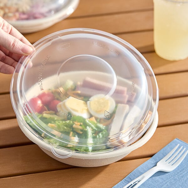 A hand putting a Dart clear plastic dome lid on a salad bowl.