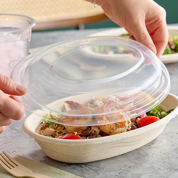 A person's hand holding a Dart clear plastic lid over a bowl of food.