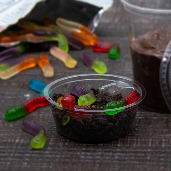 A clear plastic cup filled with gummy worms next to a clear plastic container of chocolate.