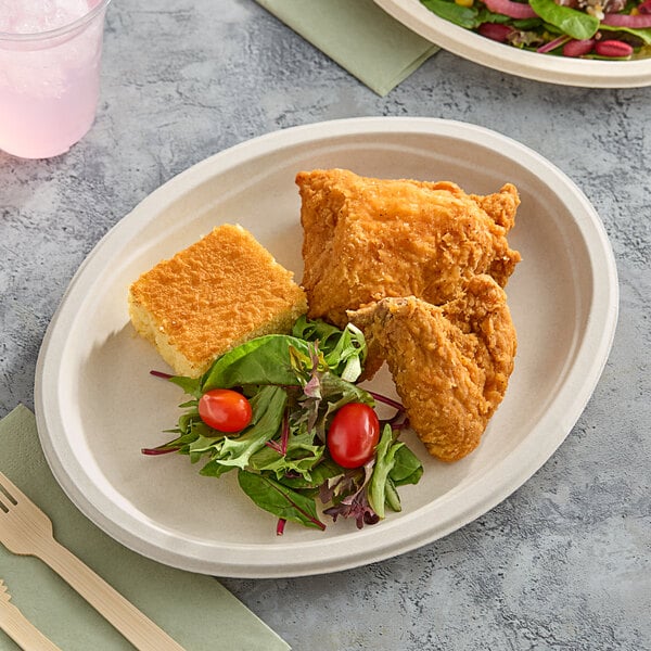 A Dart ProPlanet oval fiber platter with fried chicken and salad on a table with a wooden fork.