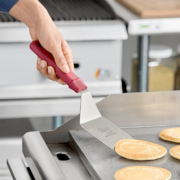 A person using a Choice beveled square edge turner with a red handle to fry a pancake.