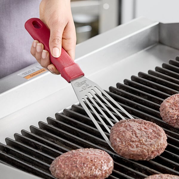A person using a Choice red fish/egg turner to grill a hamburger patty.