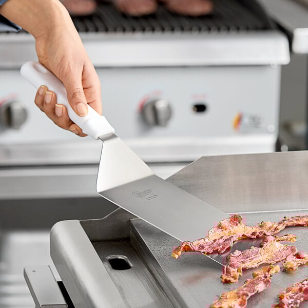 A person using a Choice square edge turner to flip bacon on a grill.