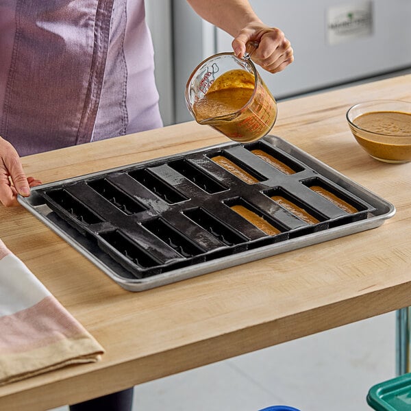 A woman pouring a brown liquid into a Sasa Demarle Flexipan scored bar mold.