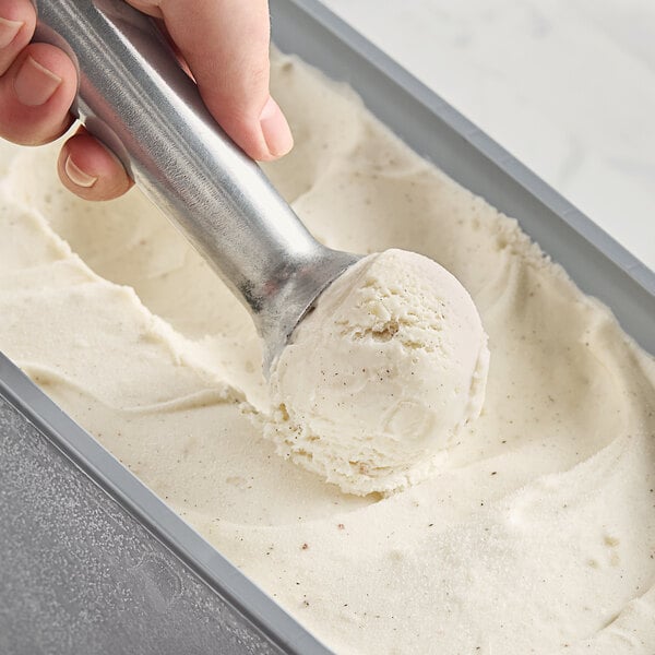 A hand scooping brown butter gelato with a silver scoop.
