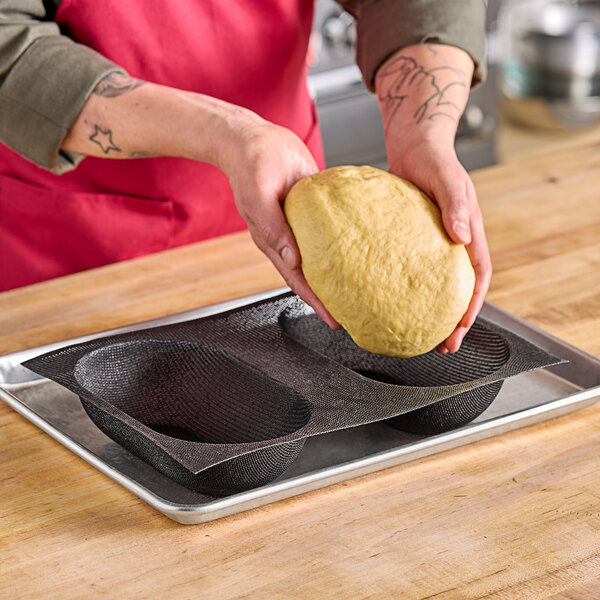 A person holding a ball of dough above a Sasa Demarle silicone oval brioche mold.