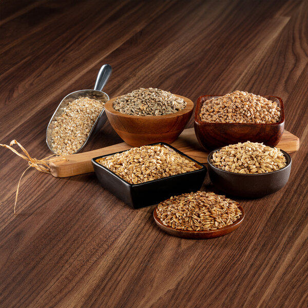 A bowl of Briess crushed rye malt on a table with bowls of different types of grain.