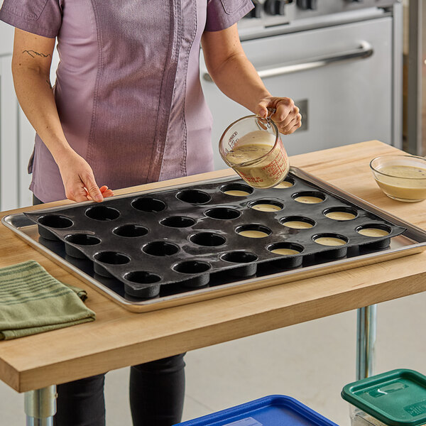 A woman pouring batter into a Sasa Demarle silicone cylinder mold with 24 holes.
