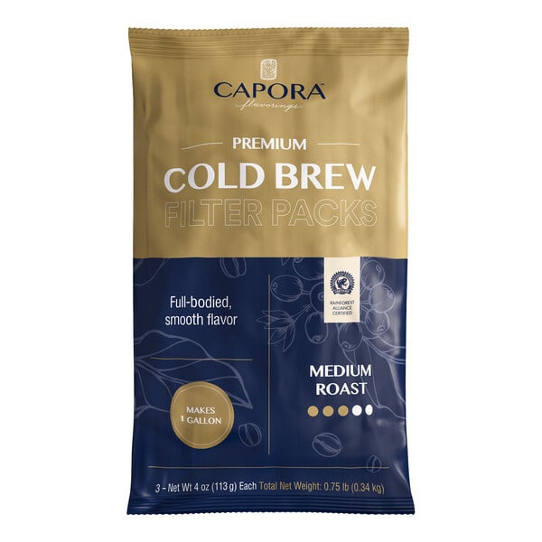 A sealed bag with gold and navy blue colors labeled 'Capora Premium Cold Brew Filter Packs' and 'Medium Roast,' featuring text and graphics indicating it makes 1 gallon and is Rainforest Alliance Certified.